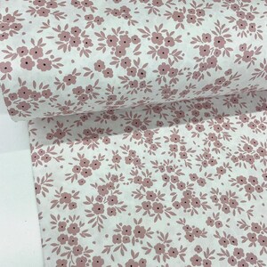 Puede incluir: Rollo de tela blanca con un patr&oacute;n repetido de peque&ntilde;os racimos florales rosas y hojas verdes. Las flores tienen centros oscuros, creando un dise&ntilde;o delicado. La tela es probablemente de algod&oacute;n o similar, adecuada para proyectos de costura o artesan&iacute;a.