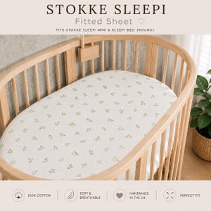 May include: A white fitted sheet with a small green leaf pattern on a round wooden crib. The text reads STOKKE SLEEPI Fitted Sheet, FITS STOKKE SLEEPI MINI & SLEEPI BED (ROUND), 100% COTTON, SOFT & BREATHABLE, HANDMADE IN THE UK, PERFECT FIT.