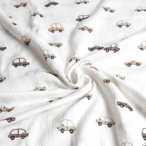 May include: White muslin fabric with a repeating pattern of small, tan and brown cars. The cars are in various styles, including sedans and trucks. The fabric is soft and has a crinkled texture, with a slight swirl in the center.