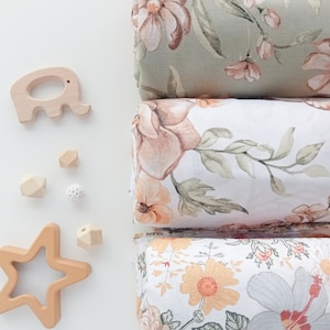 May include: Three rolls of fabric with floral patterns. The top roll is green with pink flowers, the middle roll is white with peach flowers, and the bottom roll is white with yellow and orange flowers.