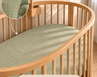 May include: An oval-shaped wooden cot with vertical slats and a light green muslin sheet. A circular inset shows a close-up of the textured, soft green fabric. The text on the image reads: Muslin Sheets For Stokke Crib, Soft, Breathable, 100% Cotton.