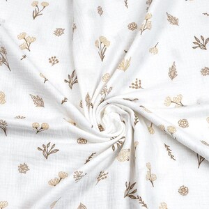May include: White fabric with a repeating pattern of tan and brown floral and leaf designs. The fabric is gathered in a swirl, showing the texture and detail of the print. The overall effect is soft and delicate.