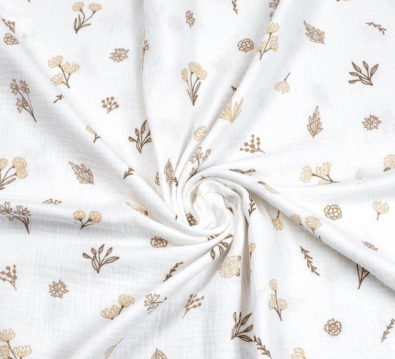 May include: White fabric with a repeating pattern of tan and brown floral and leaf designs. The fabric is gathered in a swirl, showing the texture and detail of the print. The overall effect is soft and delicate.