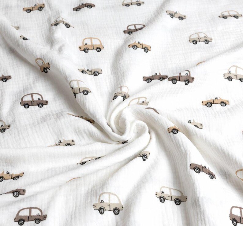 May include: White fabric with a repeating pattern of small, vintage-style cars in shades of brown and tan. The cars are evenly spaced across the soft, textured material, creating a playful and whimsical design.