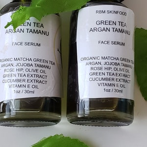 Puede incluir: Dos botellas de 30 ml de suero facial de t&eacute; verde y argan tamanu. Las botellas son de vidrio transparente con goteros negros y etiquetas blancas. Las etiquetas tienen el texto "Green Tea Argan Tamanu Face Serum" y enumeran los ingredientes: t&eacute; verde matcha org&aacute;nico, argan, jojoba tamanu, rosa mosqueta, aceite de oliva, extracto de t&eacute; verde, extracto de pepino, aceite de vitamina E.