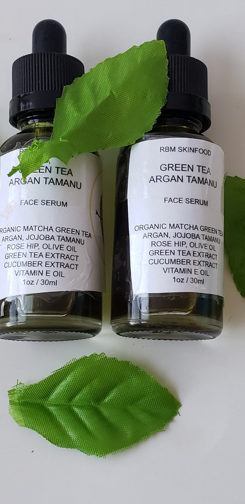Puede incluir: Dos botellas de 30 ml de suero facial de t&eacute; verde y argan tamanu. Las botellas son de vidrio transparente con goteros negros y etiquetas blancas. Las etiquetas tienen el texto "Green Tea Argan Tamanu Face Serum" y enumeran los ingredientes: t&eacute; verde matcha org&aacute;nico, argan, jojoba tamanu, rosa mosqueta, aceite de oliva, extracto de t&eacute; verde, extracto de pepino, aceite de vitamina E.