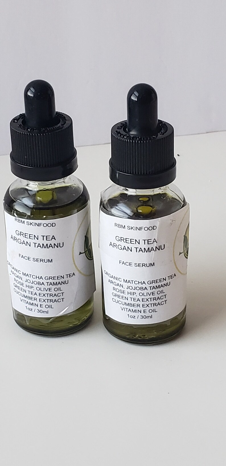 Puede incluir: Dos botellas de 30 ml de suero facial de t&eacute; verde, arg&aacute;n y tamanu. Las botellas son de vidrio transparente con goteros negros y etiquetas blancas. Las etiquetas tienen el texto "RBM SkinFood Green Tea Argan Tamanu Face Serum" y enumeran los ingredientes: "T&eacute; verde matcha org&aacute;nico, arg&aacute;n, tamanu de jojoba, rosa mosqueta, aceite de oliva, extracto de t&eacute; verde, extracto de pepino, aceite de vitamina E".