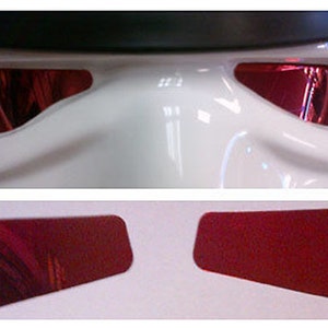 May include: Close-up of a white helmet with red-tinted eye lenses. Below, two separate red-tinted lenses are displayed. The lenses are rectangular with rounded corners. The helmet has a smooth, glossy finish.