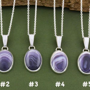 May include: Five silver necklaces with oval pendants featuring purple and white banded agate stones. Each pendant is numbered one through five at the bottom. The stones display unique swirling patterns in shades of deep violet and light lavender.