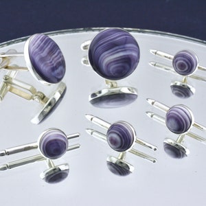 May include: A set of six silver cufflinks with purple and white shell inlays. The cufflinks are round and have a polished silver finish.