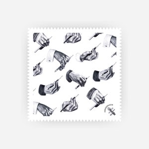 May include: A white background with a repeating pattern of black and white illustrations of hands holding pencils. The pattern is surrounded by a white border with a scalloped edge. The bottom right corner of the pattern features a black and white logo with the text "Inkermezzo".