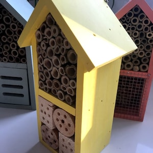 May include: A yellow wooden insect house with multiple compartments for different types of insects. The house has a variety of materials, including bamboo, wood, and pine cones.