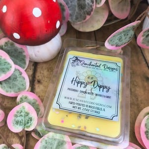 May include: A yellow wax melt in a clear plastic clamshell container with a label reading Jenchanted Designs Hippy Dippy Patchouli-Sandalwood-Berries & Mint. The label includes a cartoon flower and states Net Wt. 2.75oz (77.96g).