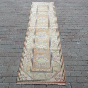 May include: A long, rectangular rug with a beige background and a colorful geometric pattern. The rug has a border with a floral design.