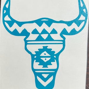 Puede incluir: Una pegatina turquesa con un diseño estilizado de calavera de toro. La calavera tiene cuernos grandes y está decorada con patrones geométricos, incluyendo zigzags y formas de diamante, creando una estética del suroeste o tribal.