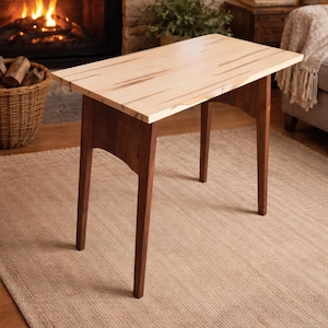 May include: A rectangular wooden side table with a light-colored top and dark brown legs. The table is approximately 30 inches long and 18 inches wide, with a height of 24 inches. The table is set on a beige rug in front of a fireplace.
