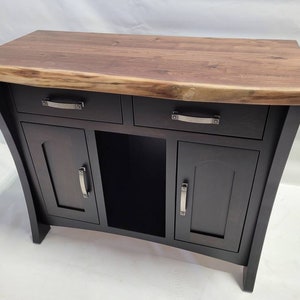 May include: A black wooden console table with a live edge walnut top. The table has two drawers and two doors with black metal hardware.
