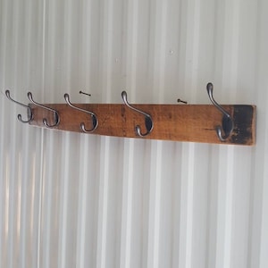 May include: A wooden coat rack with six metal hooks. The rack is made from reclaimed wood and has a rustic finish.
