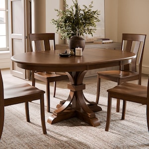 May include: A wooden dining set featuring a round table and four chairs. The table has a dark brown finish with a pedestal base. The chairs have curved backs and a matching finish. A vase with greenery and a candle are on the table.