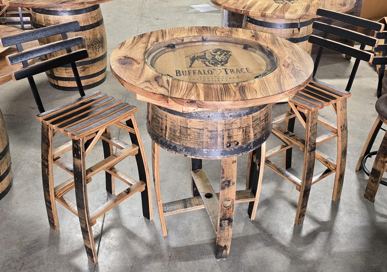 May include: A rustic, round bar table and two matching stools made from reclaimed wood. The table features a clear inset with the "Buffalo Trace" logo. The stools have slatted seats and black accents. The table is approximately 36 inches in diameter.