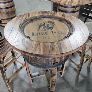 May include: A round wooden table with a glass top, featuring the "Buffalo Trace" logo. The table is supported by a repurposed barrel base and is surrounded by matching wooden chairs. The table is approximately 36 inches in diameter.
