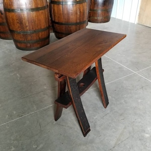 May include: A wooden table with a brown top and black legs made from repurposed wine barrels. The table is sitting on a concrete floor.