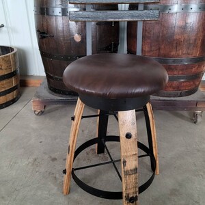 May include: A handcrafted bar stool with a brown leather seat and a backrest made of dark wood. The legs are constructed from light-colored wood and black metal. The stool is designed to complement a rustic or industrial decor.