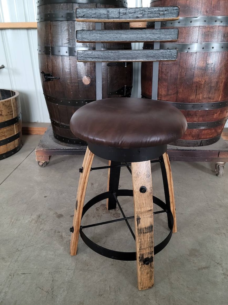 May include: A handcrafted bar stool with a brown leather seat and a backrest made of dark wood. The legs are constructed from light-colored wood and black metal. The stool is designed to complement a rustic or industrial decor.