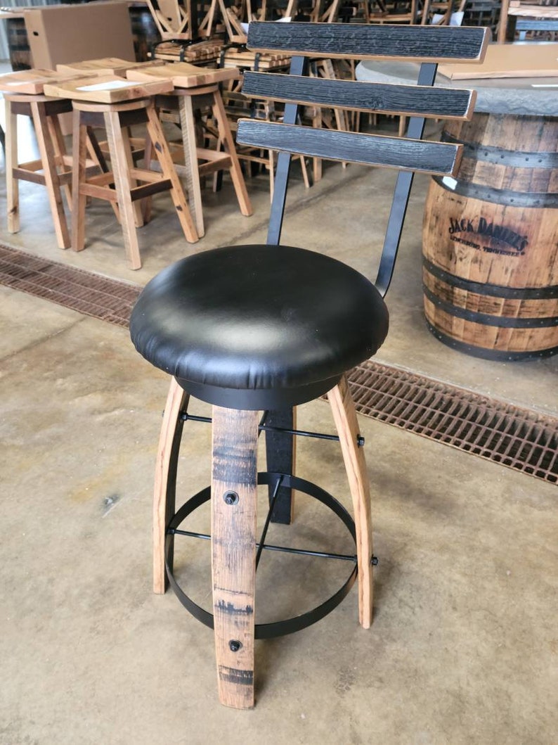 May include: A black leather seat swivel bar stool with a backrest. The stool features a black metal frame, wooden legs, and a circular footrest. The backrest has three horizontal wooden slats.