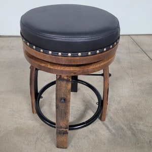 May include: A black leather-covered bar stool with a wooden base and a metal ring footrest. The stool has a studded edge around the top.