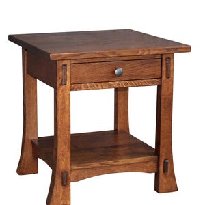 May include: A wooden side table with a square top and a drawer. The table has a lower shelf and four sturdy legs. The wood has a warm, medium brown tone, and the drawer features a small, round metal knob.