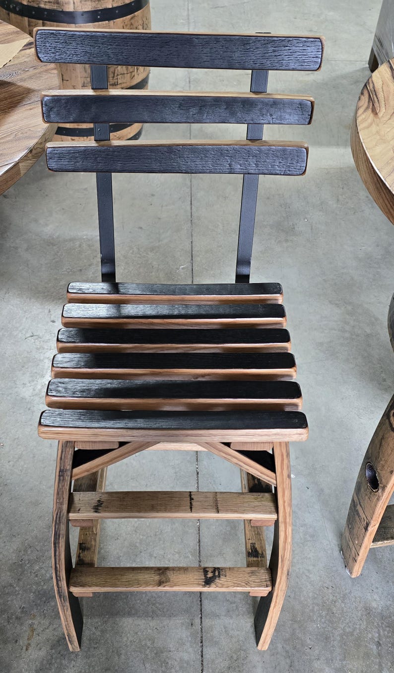 May include: A wooden chair with a slatted seat and back, constructed from repurposed barrel staves. The chair features a dark, charred finish on the slats and a natural wood tone on the frame, with metal supports. The chair is designed for indoor or outdoor use.