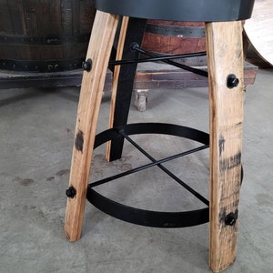 May include: A rustic bar stool with a brown leather seat and a black metal frame. The legs are made of light-colored wood with dark markings, and the footrest is a black metal ring. The stool is designed to be sturdy and stylish.