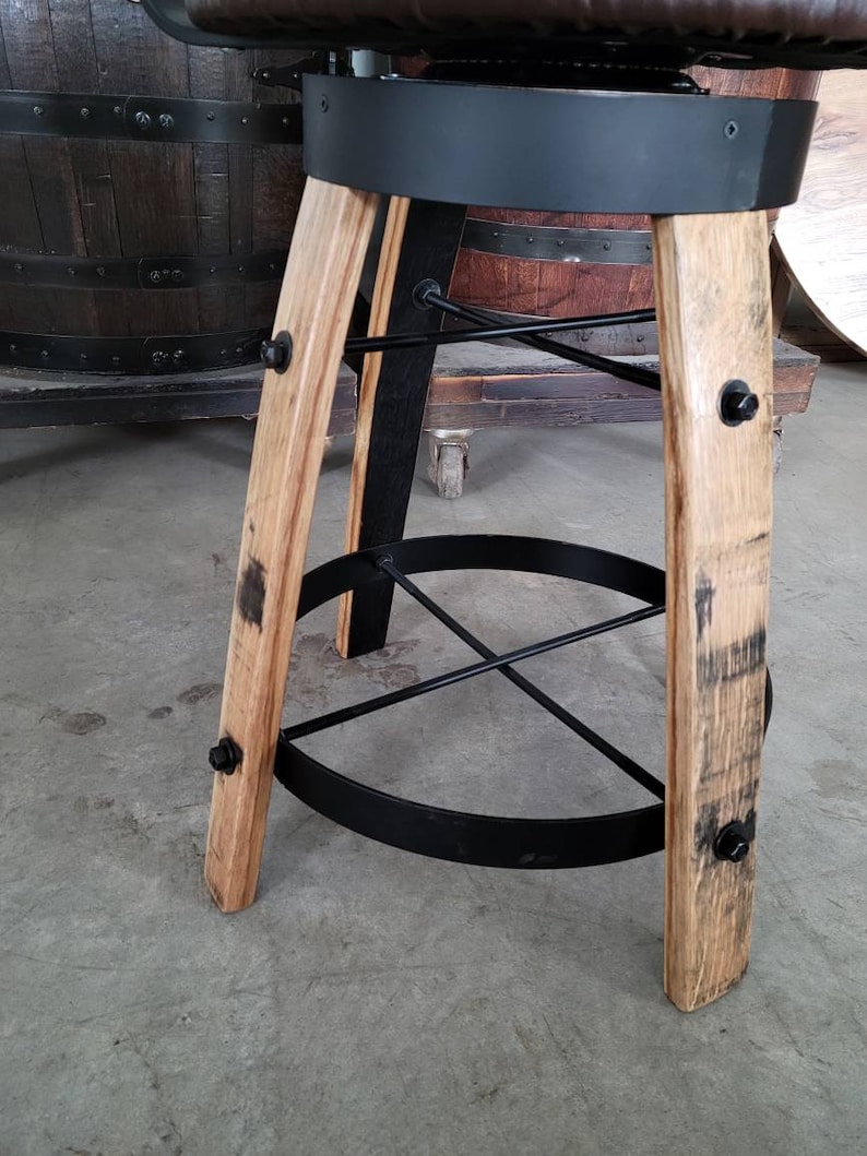 May include: A rustic bar stool with a brown leather seat and a black metal frame. The legs are made of light-colored wood with dark markings, and the footrest is a black metal ring. The stool is designed to be sturdy and stylish.