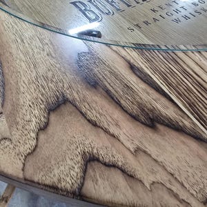 May include: Close-up of a wooden table with a glass top. The wood has a natural grain pattern with dark brown accents. The text "BUFFALO KENTUCKY STRAIGHT BOURBON WHISKEY" is visible on the wood.