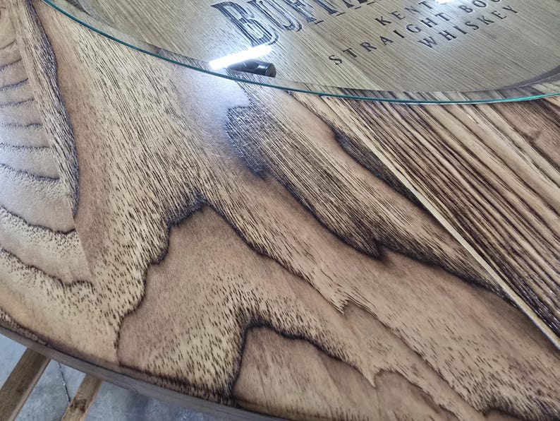 May include: Close-up of a wooden table with a glass top. The wood has a natural grain pattern with dark brown accents. The text "BUFFALO KENTUCKY STRAIGHT BOURBON WHISKEY" is visible on the wood.