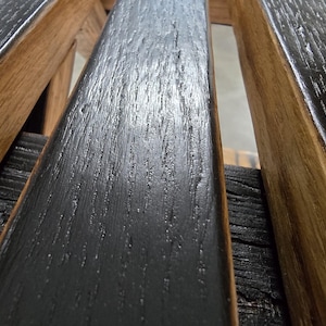May include: Close-up of a wooden structure featuring alternating black and brown planks. The black planks have a textured, weathered appearance, while the brown planks display a natural wood grain. The design suggests a rustic or industrial aesthetic.