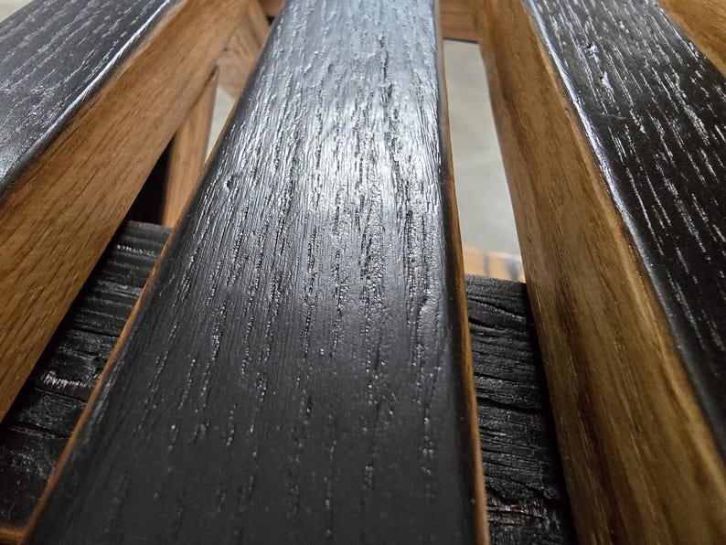 May include: Close-up of a wooden structure featuring alternating black and brown planks. The black planks have a textured, weathered appearance, while the brown planks display a natural wood grain. The design suggests a rustic or industrial aesthetic.
