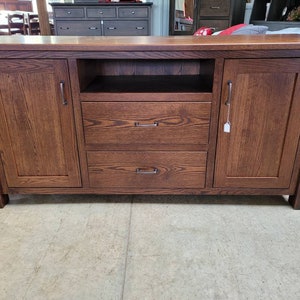 May include: A dark brown wooden entertainment center with two doors, two drawers, and an open shelf. The doors have simple, rectangular handles.