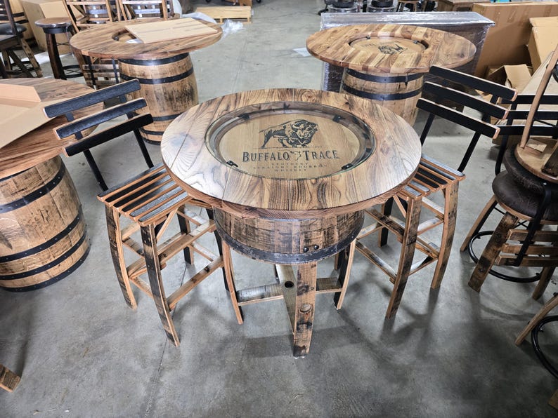 May include: Rustic wooden bar tables and stools made from repurposed barrels. The round tables feature a wooden tabletop with a recessed center, and the "Buffalo Trace" logo is visible. The stools have a slatted seat design.