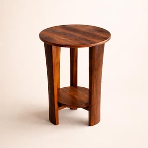 May include: A small, round wooden side table with a dark brown finish. The table has a circular top and a lower shelf, supported by four curved legs. The table is approximately 24 inches tall.