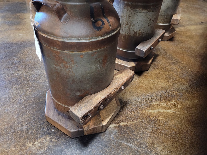 Puede incluir: Tres taburetes r&uacute;sticos de metal en forma de bid&oacute;n de leche con bases de madera. Los taburetes est&aacute;n desgastados y tienen un aspecto envejecido. Las bases son de madera reciclada y tienen un acabado natural.