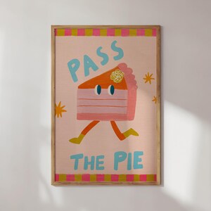 May include: A framed art print featuring a whimsical illustration of a slice of pie with legs, running. The artwork has a pink background with the words "PASS THE PIE" in blue and yellow. The frame is a light brown color.