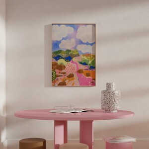 May include: A pink round table with a brown and beige stool and a pink stool. A white vase with black speckles sits on the table. A framed painting of a colorful landscape hangs on the wall behind the table.