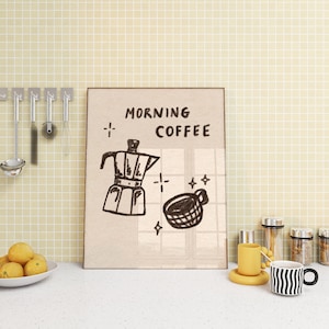 May include: A beige tiled kitchen countertop with a framed illustration of a coffee pot and a coffee cup. The illustration is titled "Morning Coffee". There are two yellow lemons and a white bowl on the counter. There are also several glass jars with lids and a yellow mug on the counter.