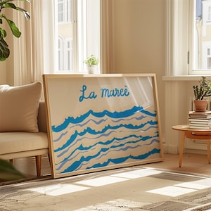 May include: A framed print with a light blue and white abstract design of waves. The print has the French text "La marée" in blue cursive writing.