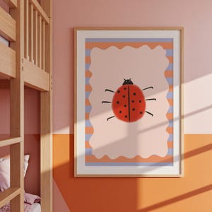 Könnte beinhalten: Gerahmter Kunstdruck mit einer Illustration eines Marienkäfers. Der rote Marienkäfer mit schwarzen Punkten ist auf einem hellrosa Hintergrund mit einem wellenförmigen orangefarbenen und violetten Rand abgebildet. Der Rahmen ist helles Holz.