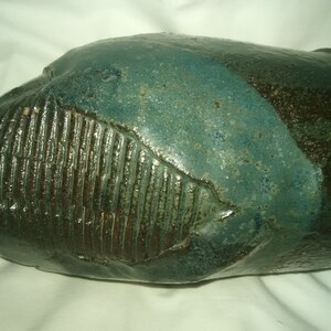 May include: A ceramic vase with a textured, dark green and brown glaze. The vase has a unique, organic shape.