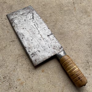 May include: A large, silver cleaver with a wooden handle. The blade is dull and has a few rust spots. The handle is wrapped in brown tape.