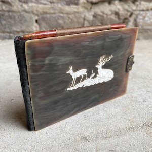Puede incluir: Un diario vintage de cuero marrón con un diseño decorativo de ciervo blanco en la portada. El diario tiene una correa de cuero marrón y un lápiz sujeto a la portada.